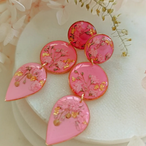 Tieto ružové visiace náušnice sú stvorené pre okamihy, keď chceš zažiariť. Jemná ružová živica pôsobí luxusne a žensky, zatiaľ čo drobné kvietky gypsomilky, plátkové zlato a nežné zelené lístky vytvárajú harmonickú, romantickú kompozíciu